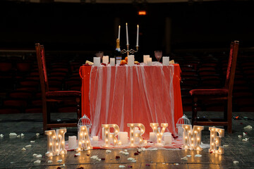 Romantic "Marry Me" Proposal Setup on Stage with Candlelit Table, Red Drapery, and Illuminated Letters