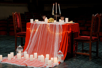 Romantic candlelit dinner setup with red tablecloth, white candles, and fairy lights on stage © Galka3250