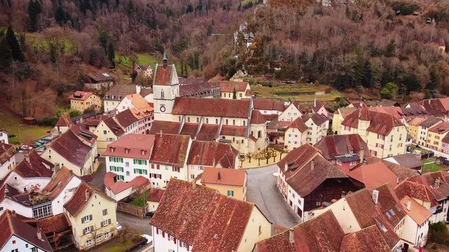 Aerial view of the church and town with red-tiled roofs nestled in a valley, surrounded by trees, Clos du Doubs, Jura, Switzerland.
