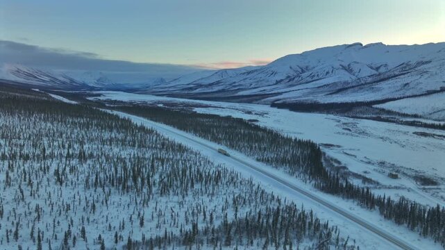 Aerial view of the Dalton Highway cuts through the snow-laden landscape of Alaska, with a lone truck traversing the icy road, Alaska, United States.