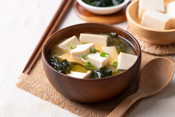 Healthy Japanese miso soup with soft tofu and seaweed in a wooden bowl, served with spoon and chopsticks