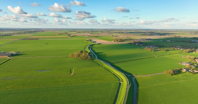 Aerial view of a winding road on a dam surrounded by fresh green fields. Drone shot of an asphalt path curving through the rural countryside on a bright sunny day. Scenic transportation infrastructure