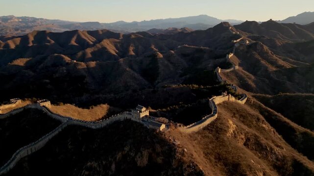 Aerial view of the winding Great Wall of China snaking across the rugged, mountainous terrain, a man-made marvel against a natural backdrop, Huairou District, China.