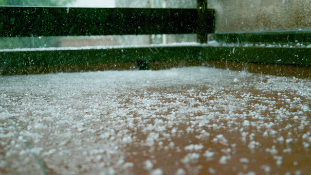 CLOSE UP, DOF: Grains of graupel and rainwater cover the brown tiled balcony.
