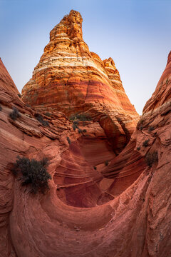 View of swirling red and orange sandstone formations rise dramatically under a clear sky, sculpted by time and elements, in Marble Canyon, Arizona, United States.