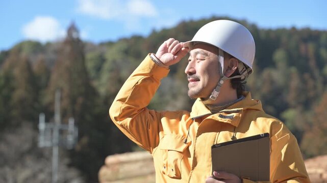 林業など第一次産業で働くヘルメットを被ったタブレットを持つ髭の中年男性の横顔　未来や目標を見つめる動画　最後にカメラ目線開発のイメージ(多摩木材センター協同組合プロパティ許可ずみ）