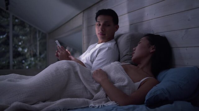 Couple in bed using smartphone, night bedroom light. Addiction social media digital technology, relationship coldness issue. Cell mobile phone scrolling problem. Useless cellphone internet surfing.