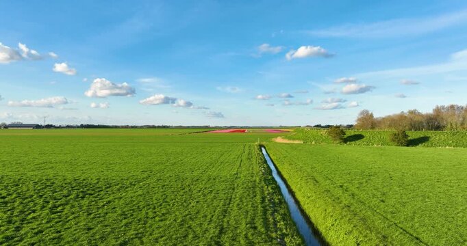 Aerial view of a water canal with sky reflection in the green countryside. Drone shot of lush pastures and meadows in a rural agricultural area on a bright sunny day. Scenic fresh landscape.