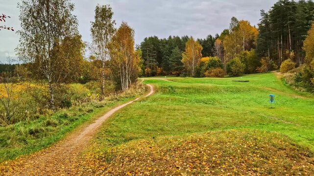 Autumn landscape featuring empty disc golf course with pathway, basket, and colorful forest
