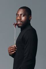 African man with dark skin wearing black turtleneck holding dried flower in creative conceptual...