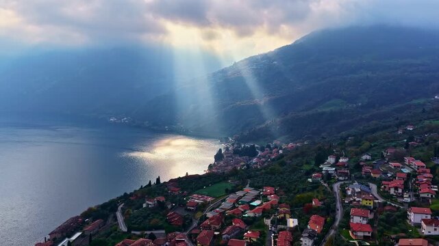The sun breaks through the clouds above Lake Iseo and the surrounding villages and mountains.