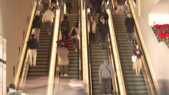 Parallel escalators with commuters moving in a busy Tokyo station.