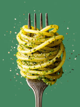 Fork Twirling Spaghetti with Green Pesto, Basil and Parmesan &ndash; Fresh Italian Pasta in Motion on White Background. Close up on Fork on Teal Green Background..