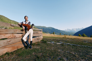 Obraz premium Woman leaning on wooden fence in countryside meadow with distant mountains, wearing riding boots and casual jacket, portrait lifestyle outdoors in wide open field under clear sky.