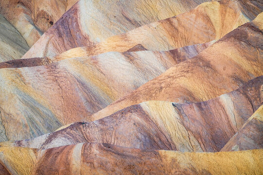 View of undulating hills painted with strokes of warm yellows, oranges, and soft purples in a mesmerizing desert landscape, Stovepipe Wells, CA, United States.
