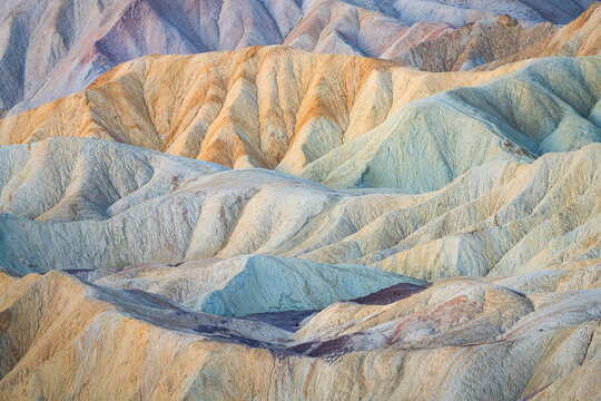 View of undulating hills displaying a tapestry of colors from pale yellow to soft blues and purples, creating a surreal desert landscape, Stovepipe Wells, CA, United States.