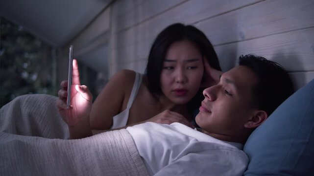 Couple in bed using smartphone, night bedroom light. Addiction social media digital technology, relationship coldness issue. Cell mobile phone scrolling problem. Useless cellphone internet surfing.