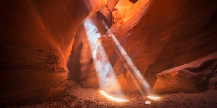 View of ethereal light beams pierce through the sinuous, red rock canyon, illuminating the sandy floor with a warm glow, Escalante, Utah, United States.