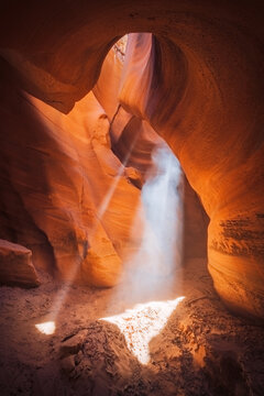 View of ethereal sunlight piercing through the sculpted sandstone slot canyon, illuminating dust motes in a mesmerizing display of light and shadow, Escalante, Utah, United States.