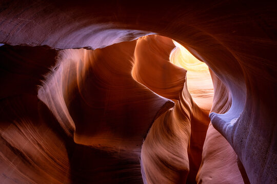 View of sculpted sandstone walls glow with ethereal light, creating a mesmerizing dance of shadows and colors in a natural cathedral, Escalante, Utah, United States.
