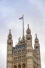 Gothic Revival tower of the Palace of Westminster (Houses of Parliament) with the Union Jack flying on a flagpole against a cloudy sky. London, England, United Kingdom