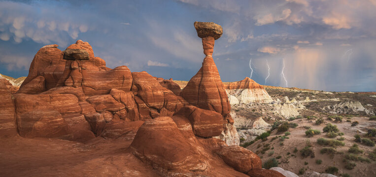View of a sandstone landscape with balanced rock formations under a stormy sky punctuated by bright lightning strikes, Escalante, Utah, United States.