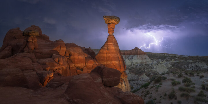 View of towering red rock formations under a dramatic sky illuminated by a bright lightning strike over the desert landscape, Escalante, Utah, United States.