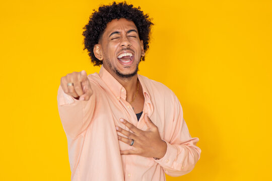 young latino man with afro hair isolated on white background pointing and laughing out loud