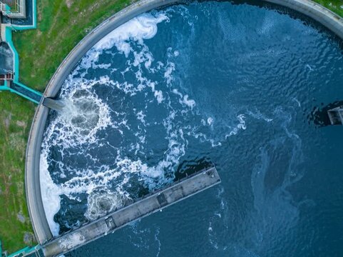 Aerial top-down view of a circular clarifier tank with swirling treated water, part of a modern wastewater treatment plant designed for sedimentation and separation processes.