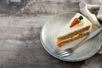 Carrot cake slice with cream cheese frosting on wooden table. Copy space