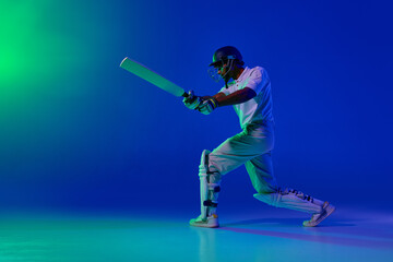 Fototapeta premium Cricket batsman forward attacking shot under blue green studio light. Concept of batting power training, motion control drills, professional cricket coaching content, dynamic sports advertising visual