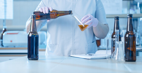 Worker chemist of brewing beer in laboratory setting with bottles and beaker