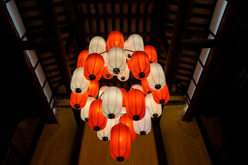 Cluster of red and white paper lanterns hanging from traditional wooden ceiling, creating warm ambient lighting in Asian interior architecture.