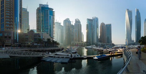 Evening view of a river canal and a ship. Orange sunlight, skyscrapers, buildings and the embankment. On the streets of the Emirates, in a public place. © Tatiana