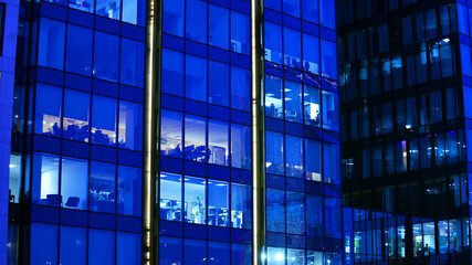 Big glowing windows in modern office building at night, in rows of windows light shines. Fragment of the glass facade of a modern corporate building at night. Modern glass office  in city.