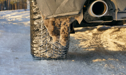 A close up photo of wet snow sticking to a car bumper and a snow clogged wheel 