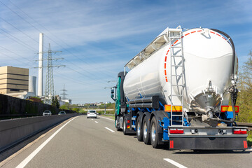 Naklejka premium White big modern tanker shipment cargo commercial semi trailer truck moving fast on motorway road city urban suburb. Business distribution logistics service. Lorry driving highway sunny day blue sky