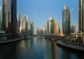 Naklejka premium Evening view of the city. Orange sunlight, skyscrapers, buildings, and city streets. On the streets of the Emirates, in a public space.