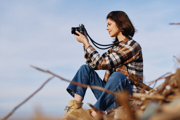 Woman photographer sits among dry branches, holding a camera for outdoor nature photography in a...