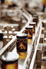Elegant stainless steel conveyor belt carries sealed brown glass cosmetic jars in a factory. Soft lighting enhances the clean production atmosphere