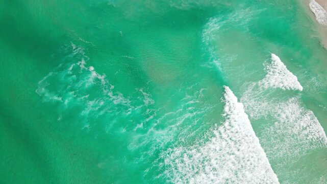 Aerial view of the turquoise ocean meeting the sandy beach with foamy waves, a serene coastal scene, Betty's Bay, Western Cape, South Africa.