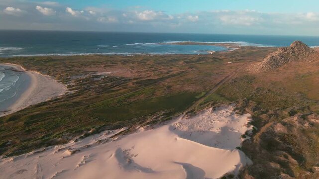 Aerial view of the coastline with sandy beach, rocky outcrop, and distant island under a serene sky, Betty's Bay, Western Cape, South Africa.