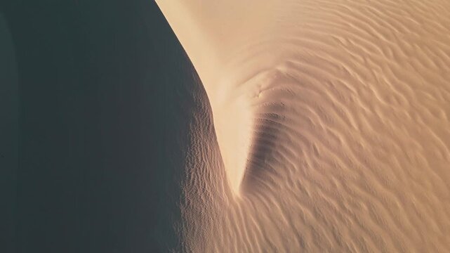 Aerial view of an expansive sand dune, where light and shadow play across the undulating surface, creating a rippled texture, Betty's Bay, Western Cape, South Africa.