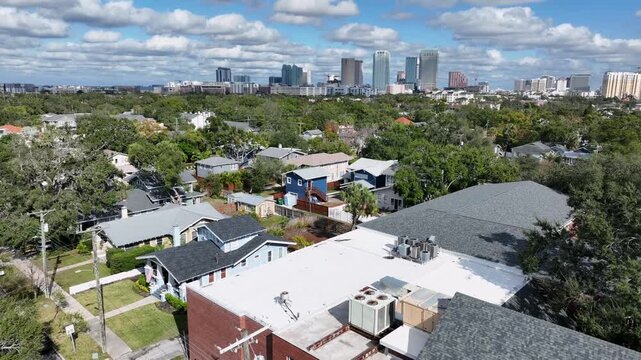 Hyde Park neighborhood in Tampa, Florida. Lush tree-lined streets, residential buildings and palm trees. Downtown Tampa skyline in distance. Aerial forward wide shot. Walking pedestrian on sidewalk.