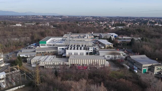 Aerial view of an industrial zone showing large manufacturing buildings, warehouses, internal roads, and surrounding woodland at the edge of an urbanized area.