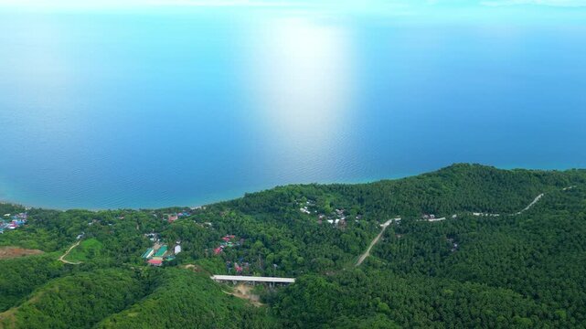 High-angle push-in aerial revealing the long white bridge of Lobo, Batangas, extending toward the sea with a vast horizon and lush green valley.
