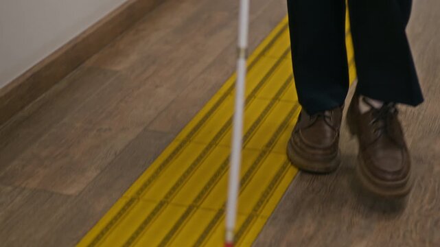 Tilt down shot of unrecognizable blind man in casualwear walking confidently using cane while visiting public library