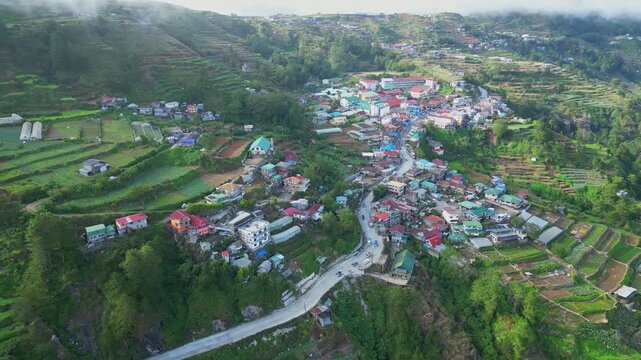Sideward pan of the town of Atok, Benguet, showcasing the densely clustered buildings along the ridges, flanked by vast, tiered rice terraces.
