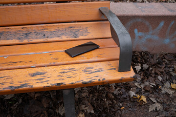 Smartphone resting on a light wooden park bench outdoors. Everyday scene showing a personal device, representing technology, leisure, and casual outdoor life.