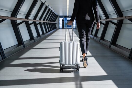 Professional business woman walking with a rolling suitcase through a modern airport skybridge with copy space for corporate travel concept.